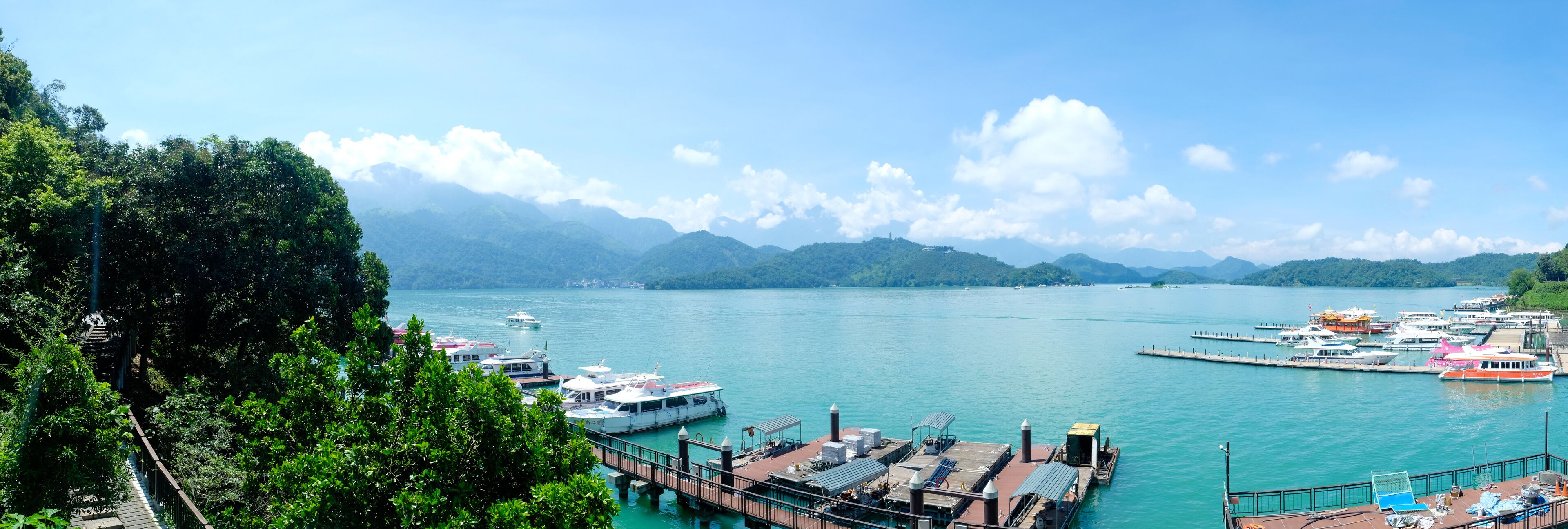 A marina with boats docked, surrounded by lush greenery and mountains in the background.