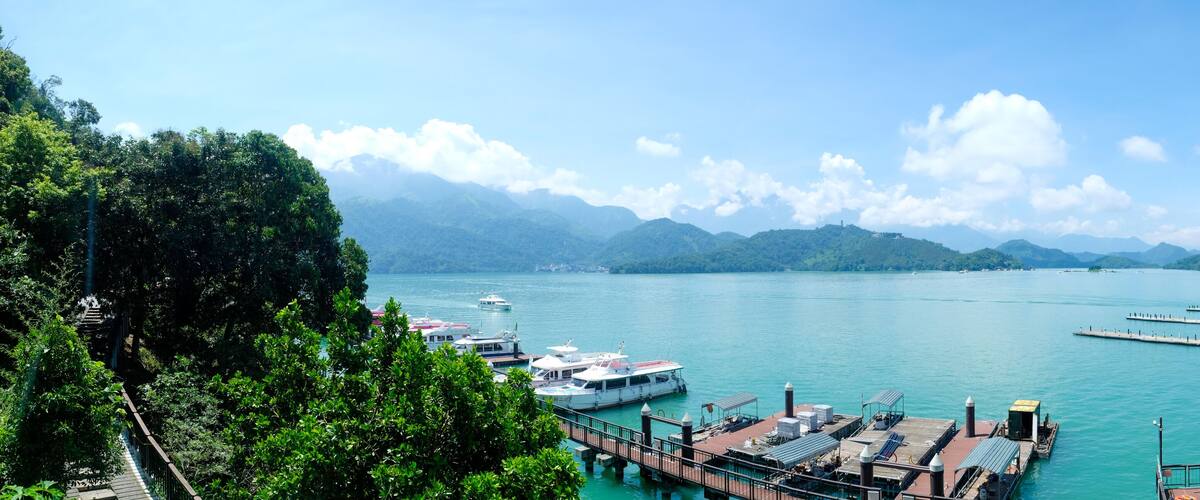 A marina with boats docked, surrounded by lush greenery and mountains in the background.
