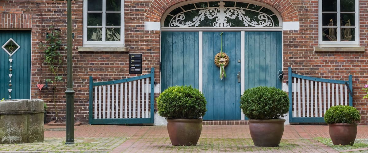 A brick building with a blue door, two potted plants, and a street lamp.