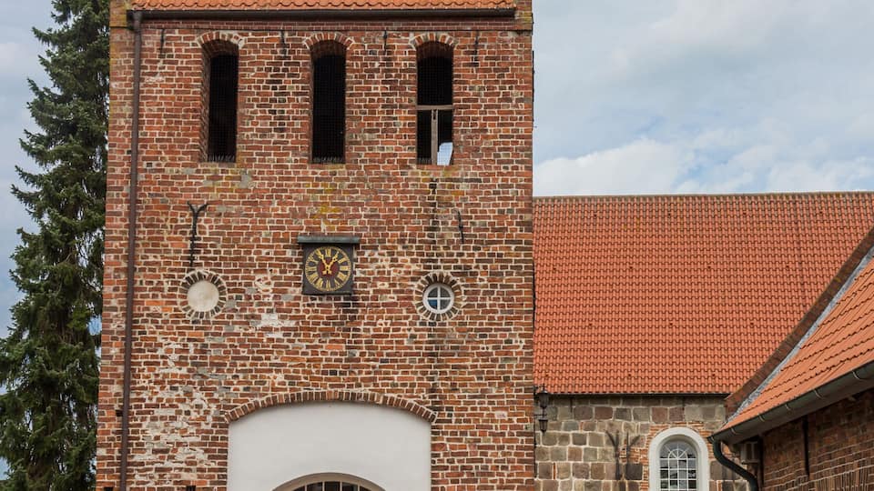 A historic brick tower with a clock, a green arched entrance, and a red-tiled roof.