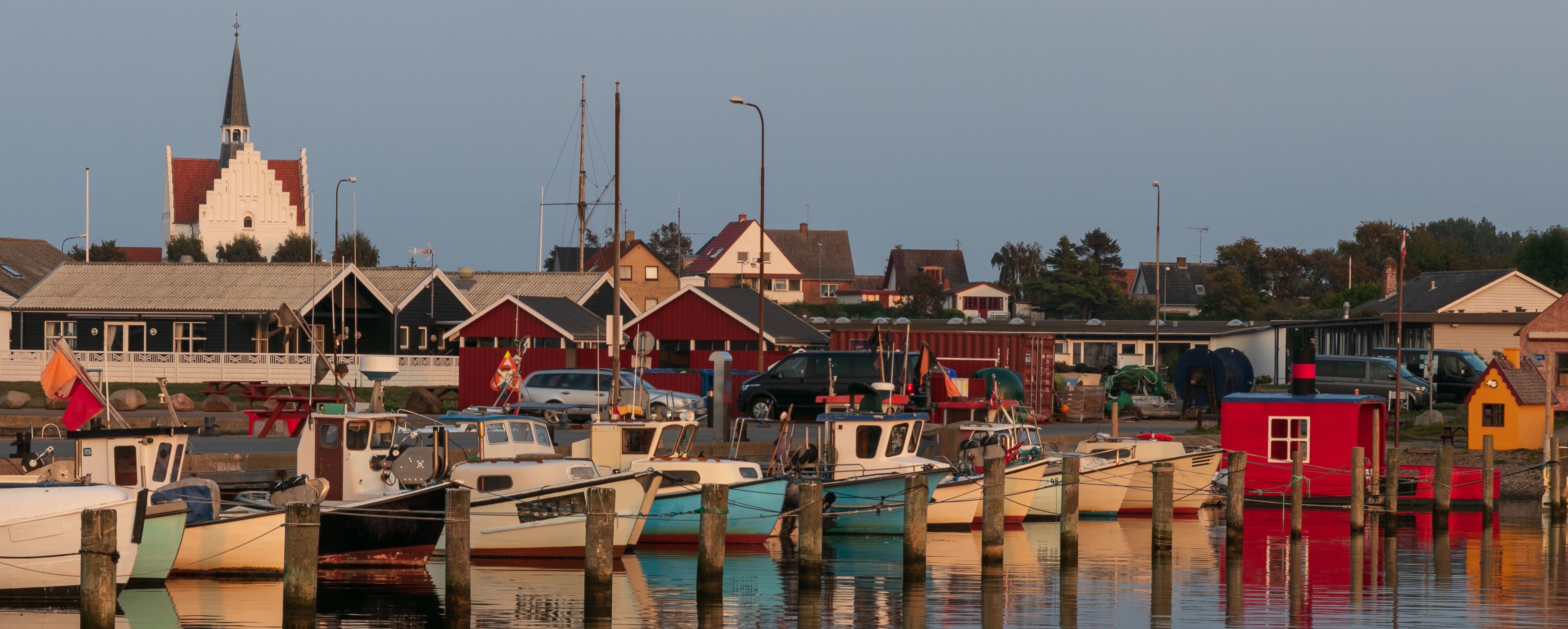 A harbor with boats docked, a church with a steeple, and houses in the background.