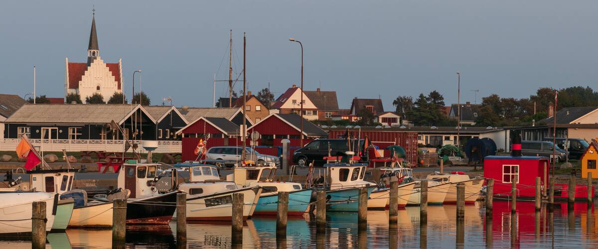 A harbor with boats docked, a church with a steeple, and houses in the background.