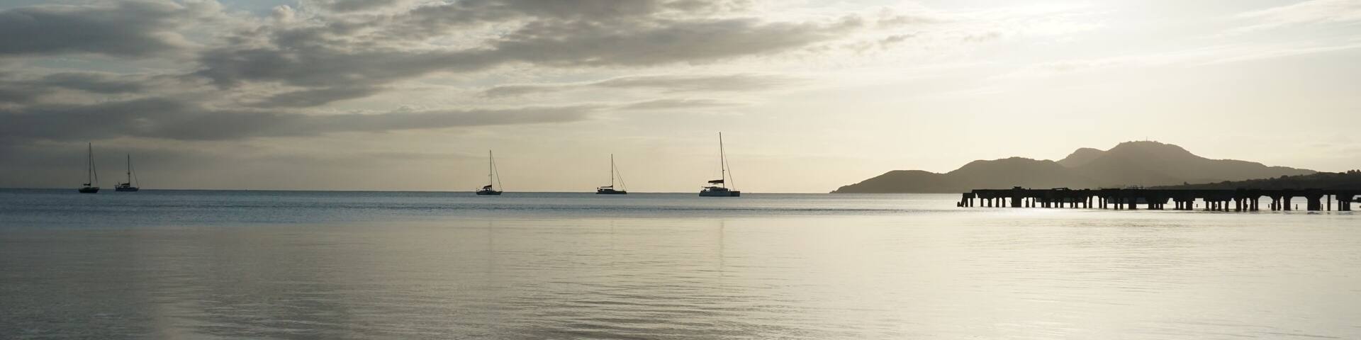 A calm sea with sailboats and a pier in the distance.