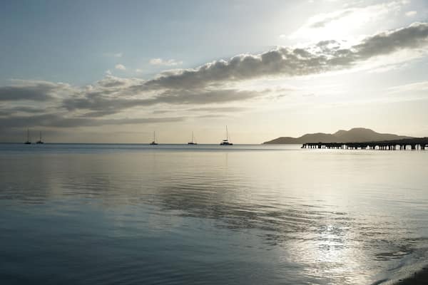 A calm sea with sailboats and a pier in the distance.