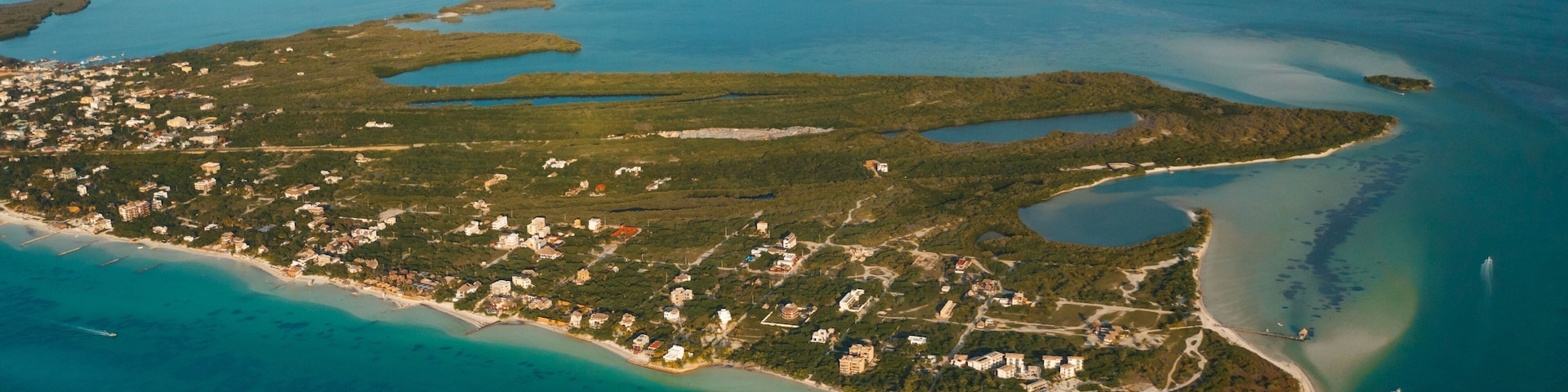 Vista aérea de una isla costera con aguas azules cristalinas, una playa de arena y edificios dispersos.