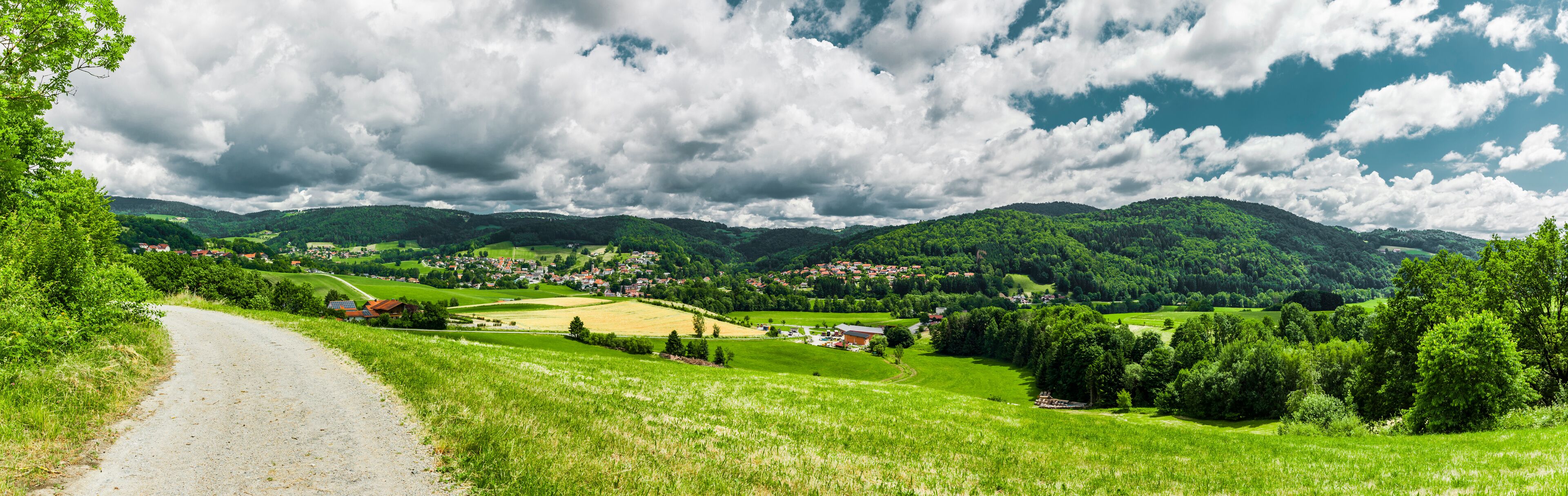A rural landscape with a winding road, green fields, and a village nestled among hills.