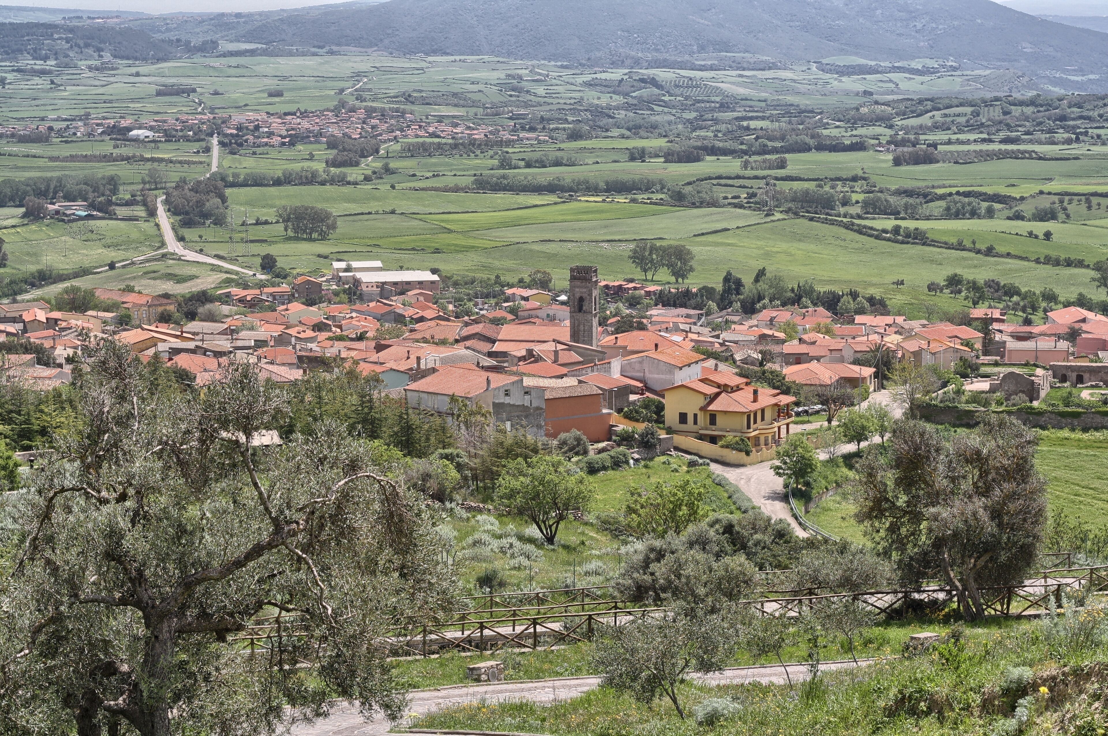 A village with red-roofed houses, a prominent tower, and surrounding green fields.
