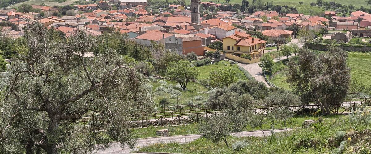 A village with red-roofed houses, a prominent tower, and surrounding green fields.