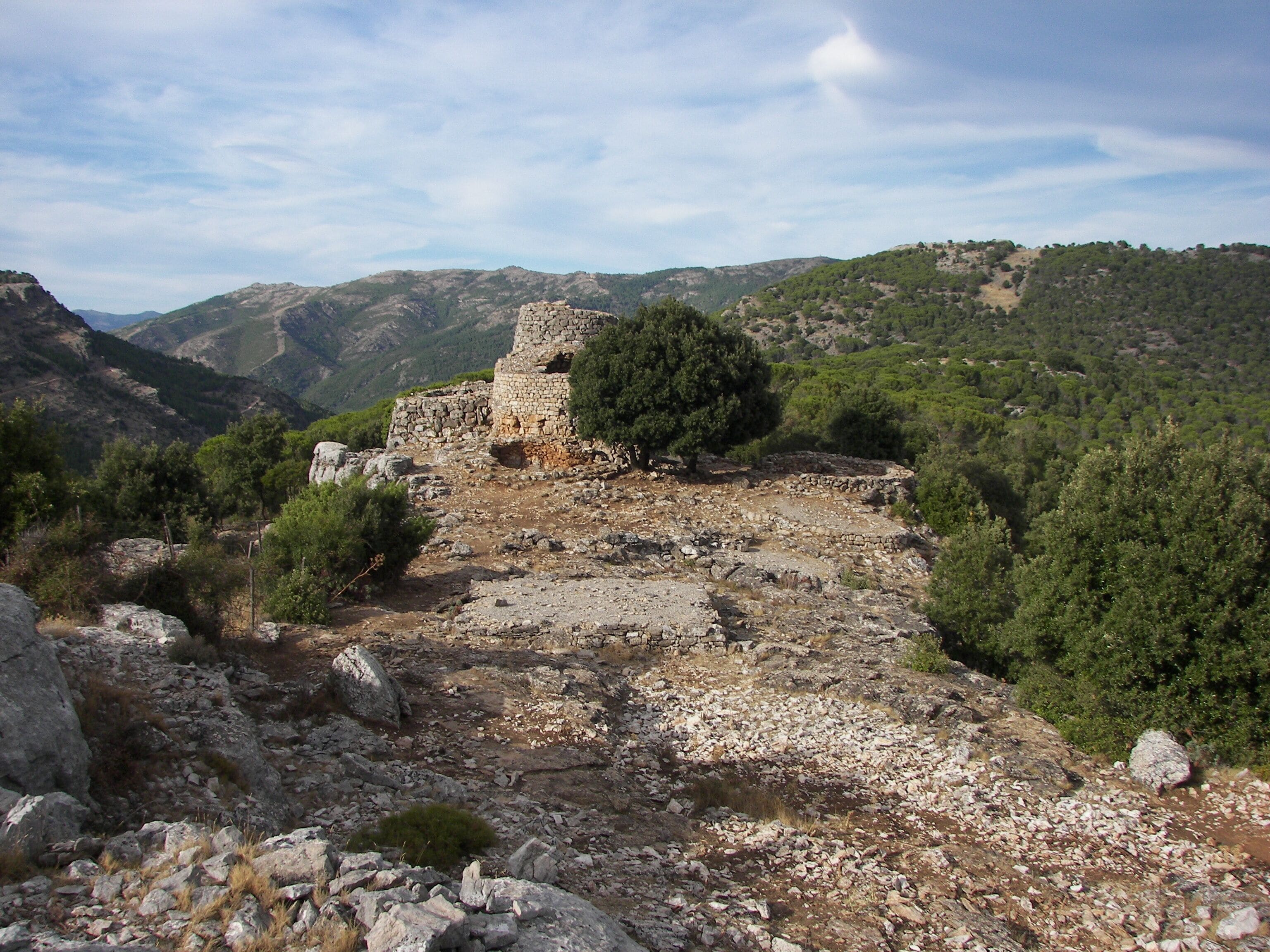 A stone ruin surrounded by a mountainous landscape with dense forests.
