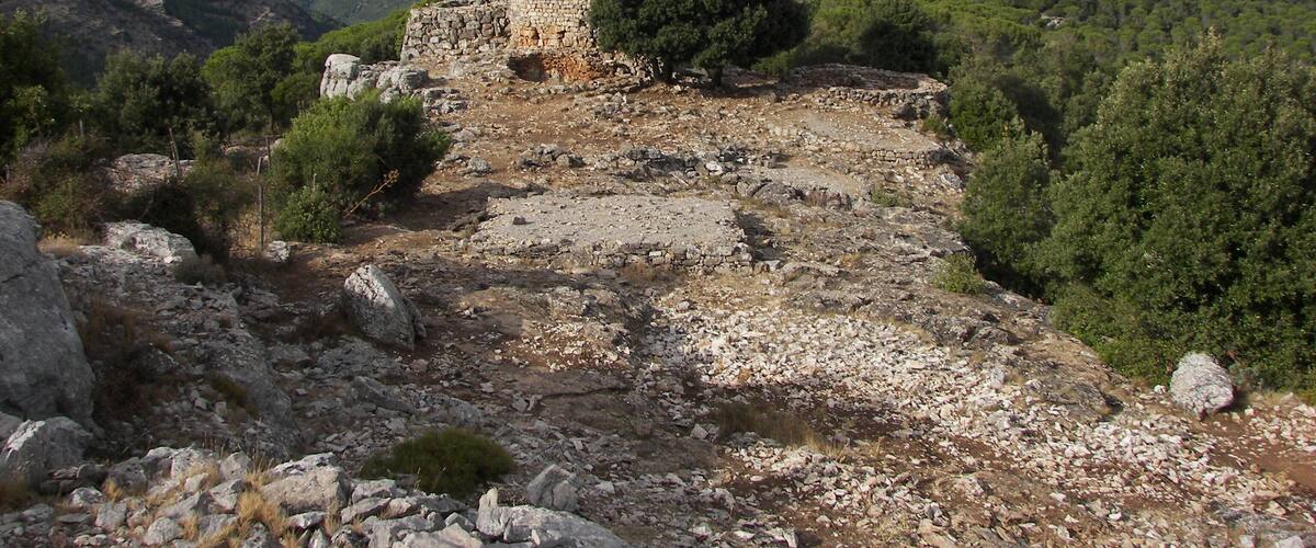 A stone ruin surrounded by a mountainous landscape with dense forests.