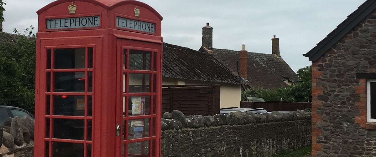 A red telephone booth with 'TELEPHONE' signs, a stone wall, and a stone building in the background.