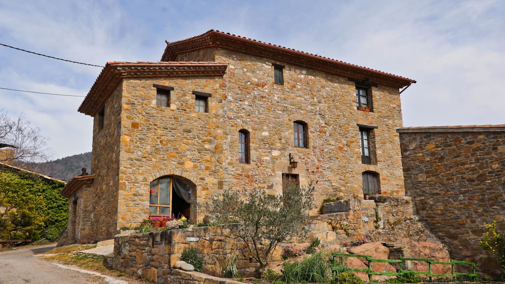 A stone building with a red-tiled roof, a small arched entrance, and a stone staircase leading up to the entrance.