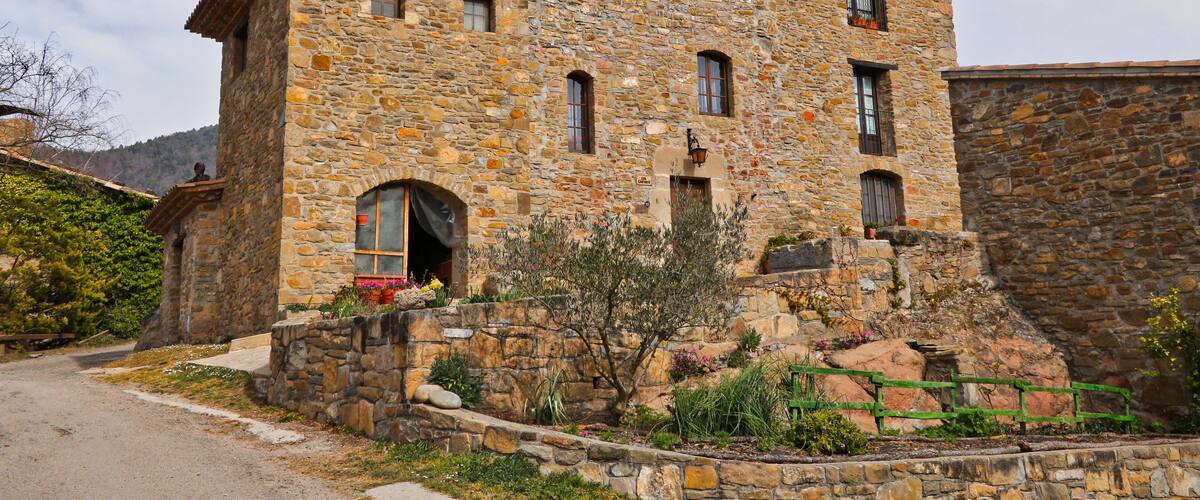 A stone building with a red-tiled roof, a small arched entrance, and a stone staircase leading up to the entrance.