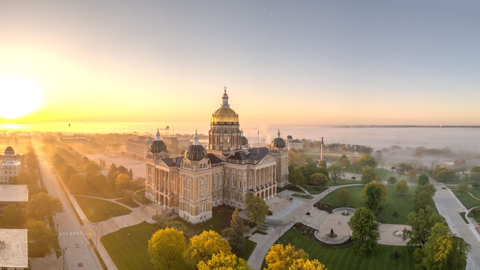A grand building with domes, surrounded by a park and a river.