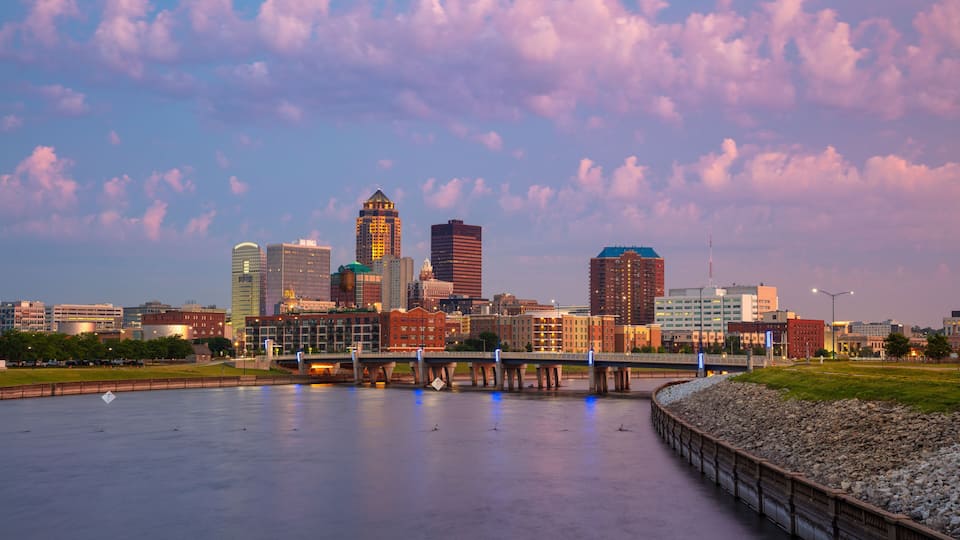 A city skyline with a river in the foreground and a bridge crossing it.