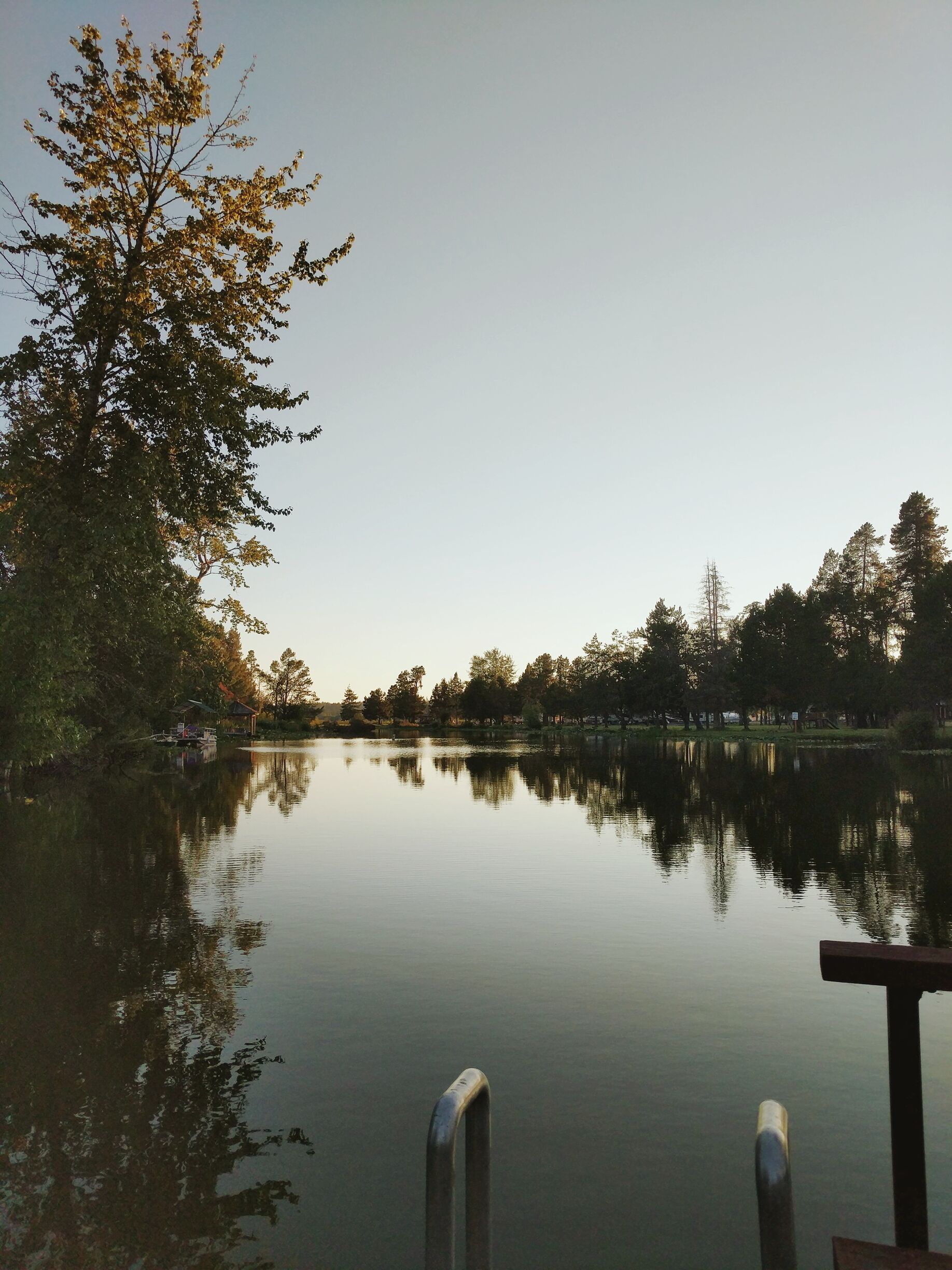 A calm lake with a dock and trees reflecting on the water.