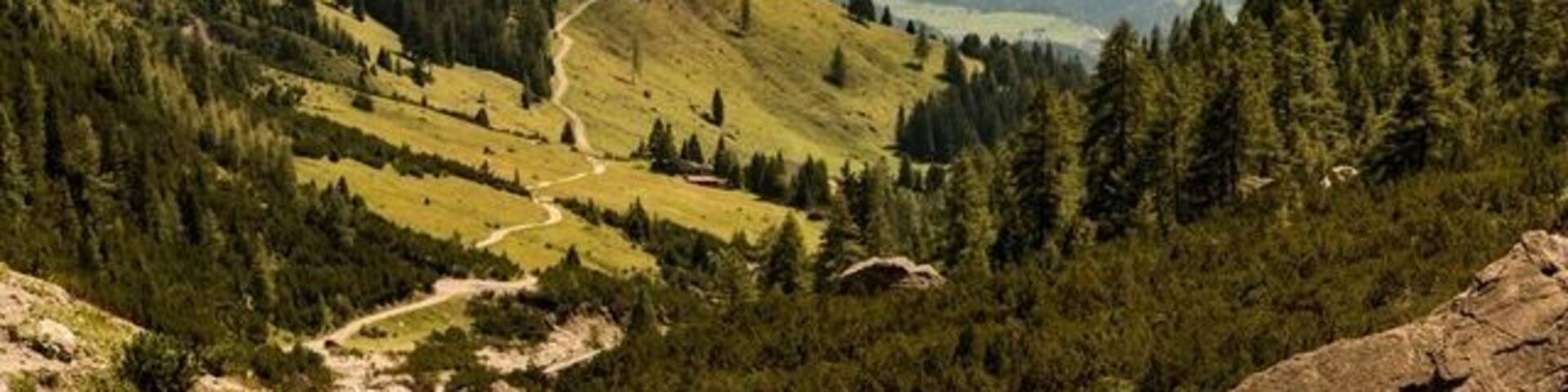 A mountain valley with a winding road, dense forests, and a lake.