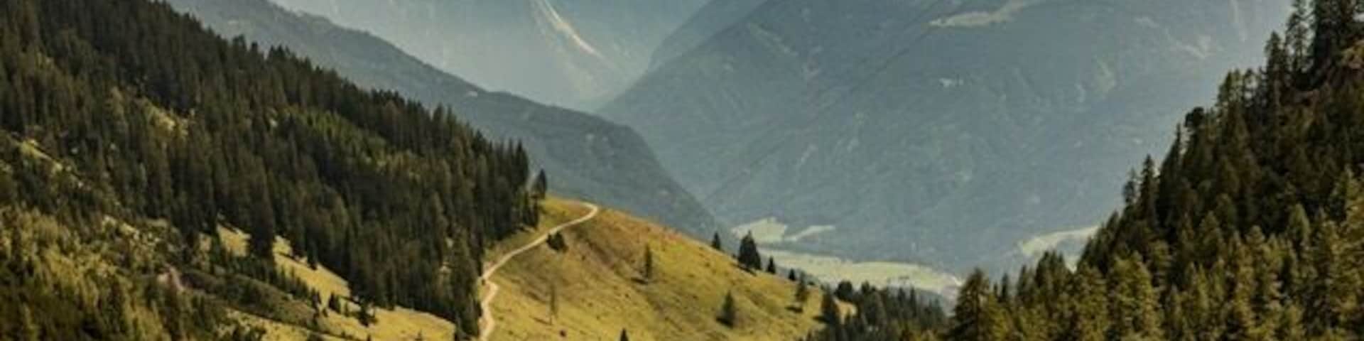 A mountain valley with a winding road, dense forests, and a lake.