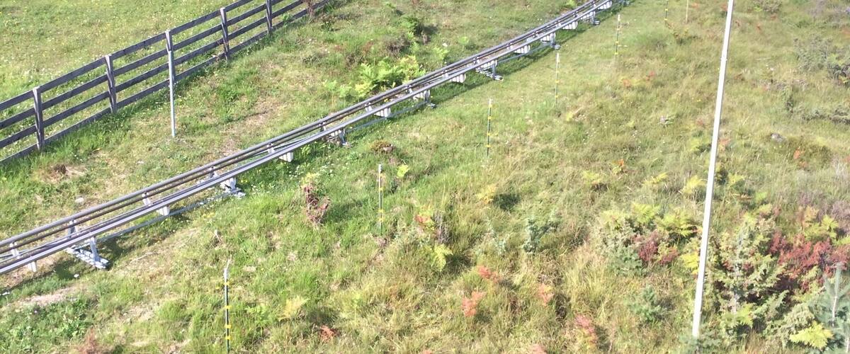 A ski lift in a mountainous area with a wooden fence and a grassy field.