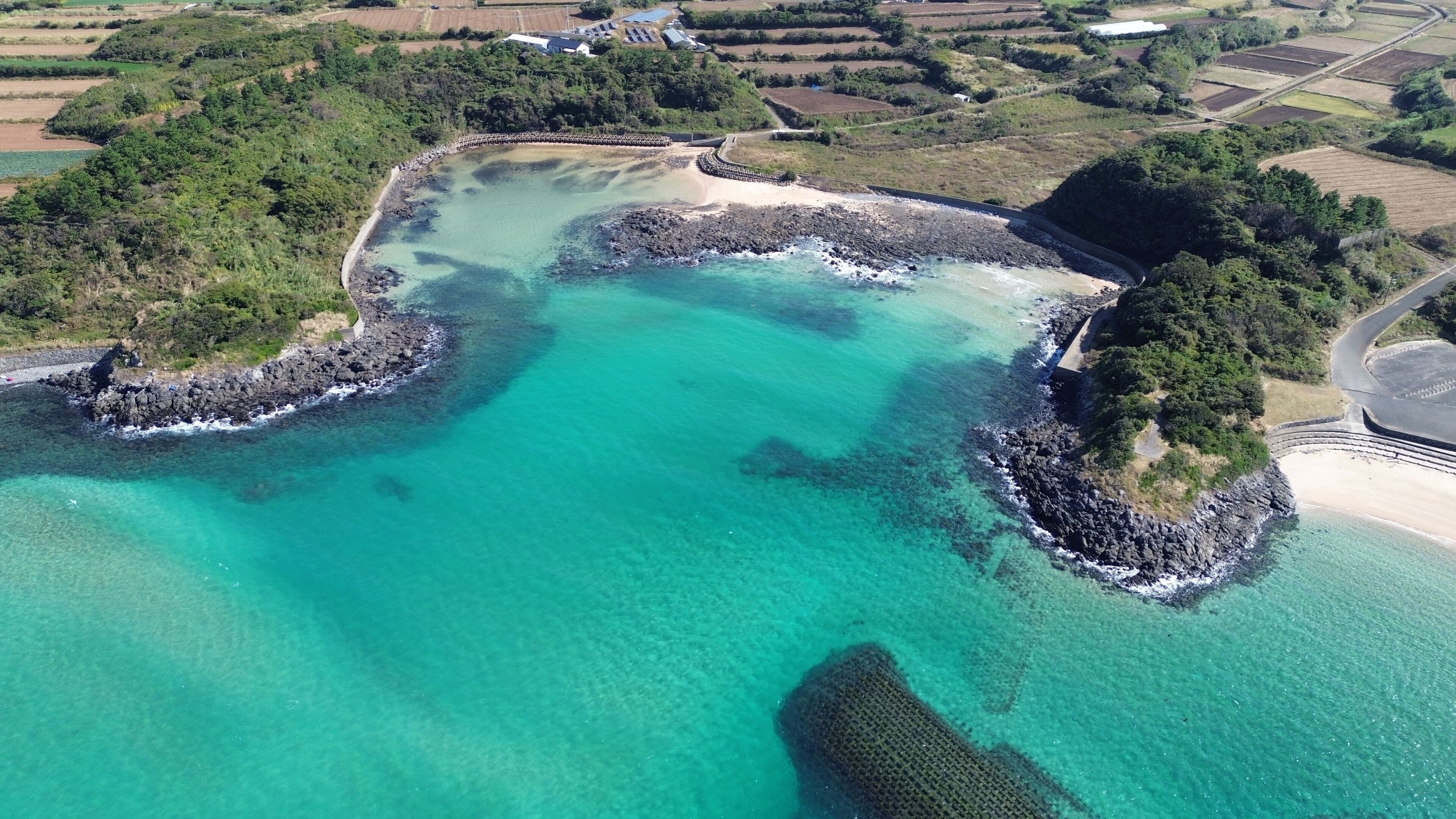 An aerial view of a coastal area with clear turquoise waters, rocky shorelines, and surrounding greenery.