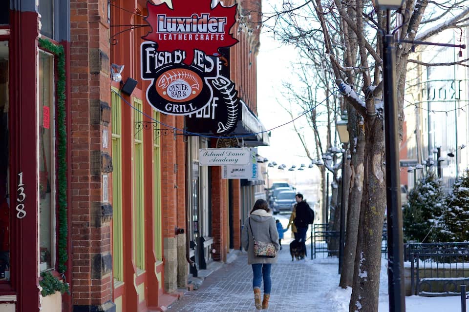 A snowy street with storefronts, including a fish and oyster bar, and a dance academy.