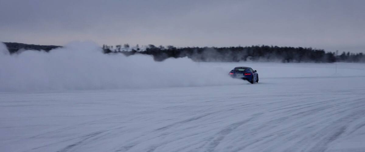 A car driving on a snowy road with tire tracks.