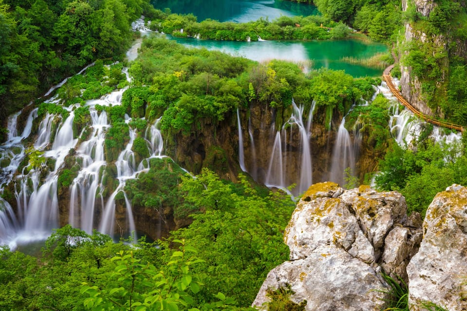 A multi-tiered waterfall surrounded by lush greenery and rocky outcrops.