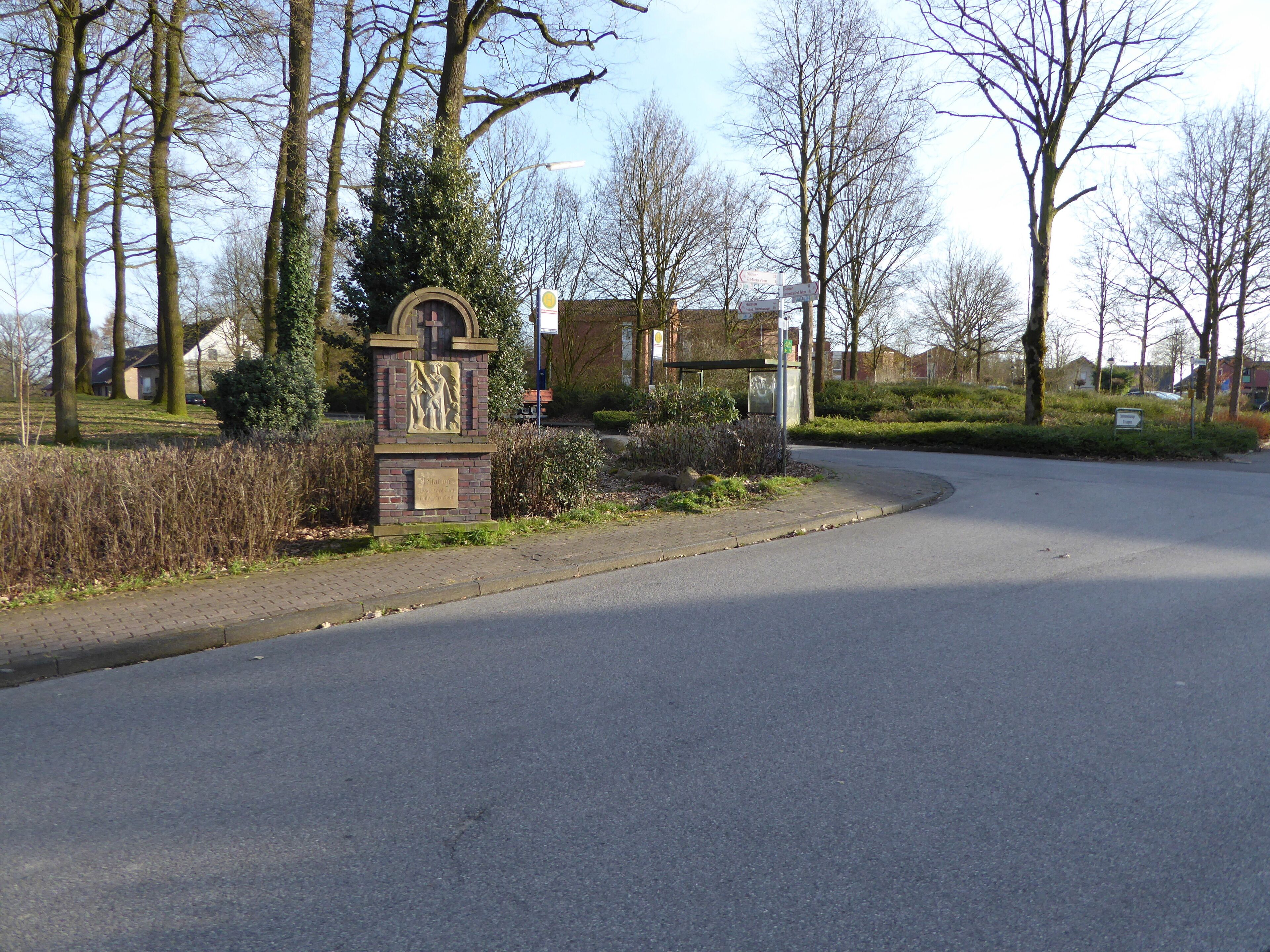 A road curving to the right with a stone monument and a bus stop sign in the foreground.