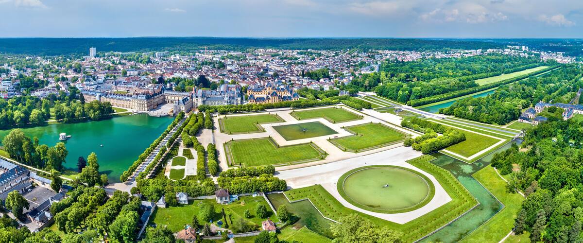 An aerial view of a city with a large palace complex, a river, and surrounding greenery.