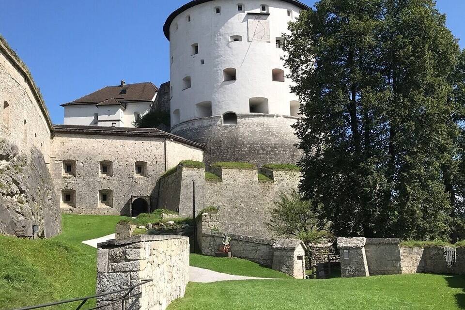 A historic castle with a round tower, stone walls, and a large tree in the foreground.