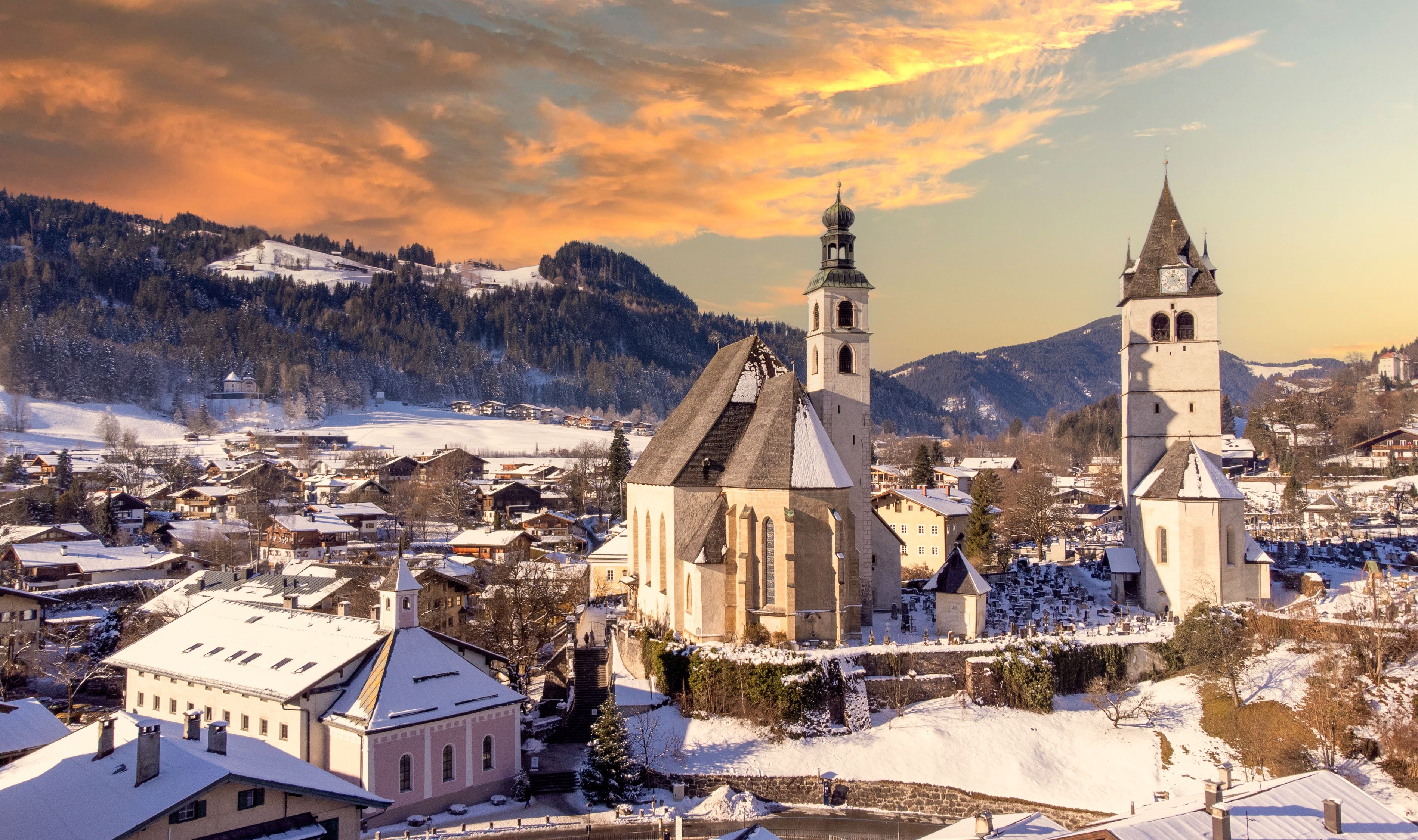 A snow-covered town with a prominent church and a tall tower, surrounded by mountains.