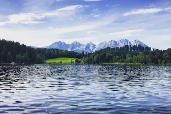 A calm lake with a forested shoreline and snow-capped mountains in the background.