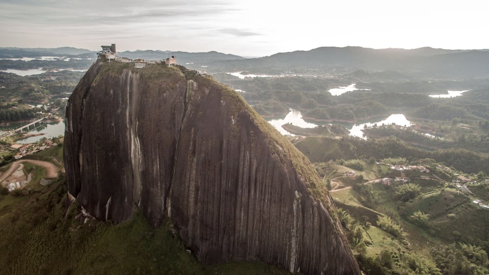 A large rock formation with a viewing platform at the top, surrounded by lush green hills and a river.