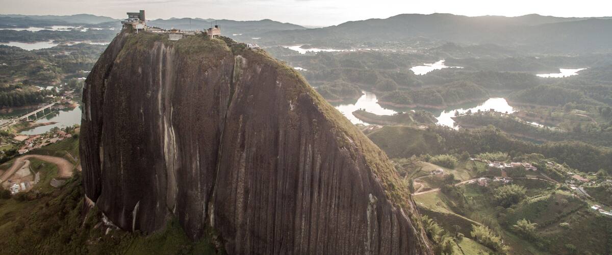 A large rock formation with a viewing platform at the top, surrounded by lush green hills and a river.