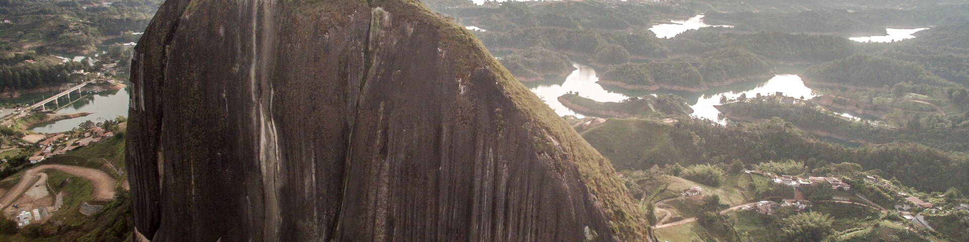 A large rock formation with a viewing platform at the top, surrounded by lush green hills and a river.