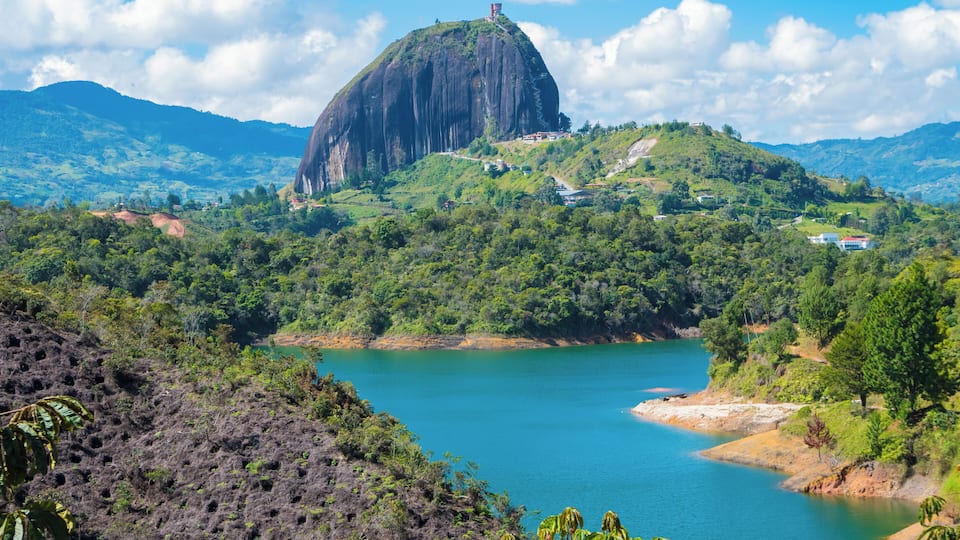 A large rock formation surrounded by lush greenery and a turquoise lake.
