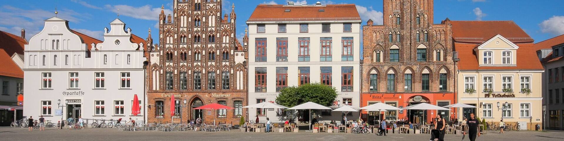 A historic square with Gothic and Renaissance architecture, including a church and cafes.