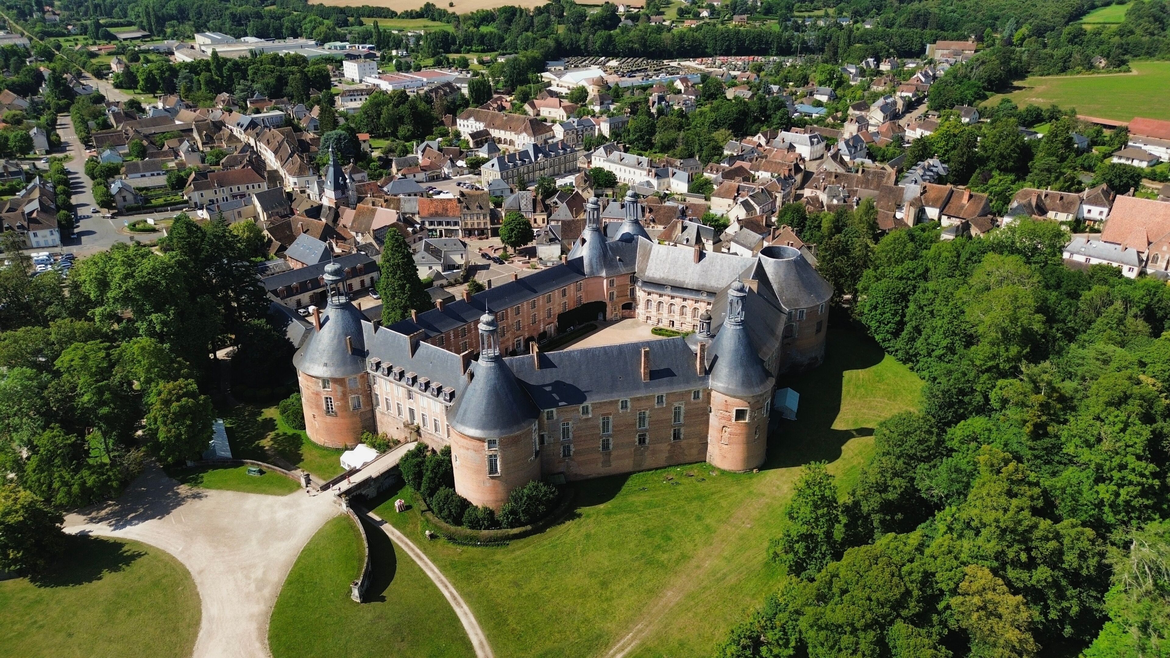 An aerial view of a historic castle surrounded by lush greenery and a small town.