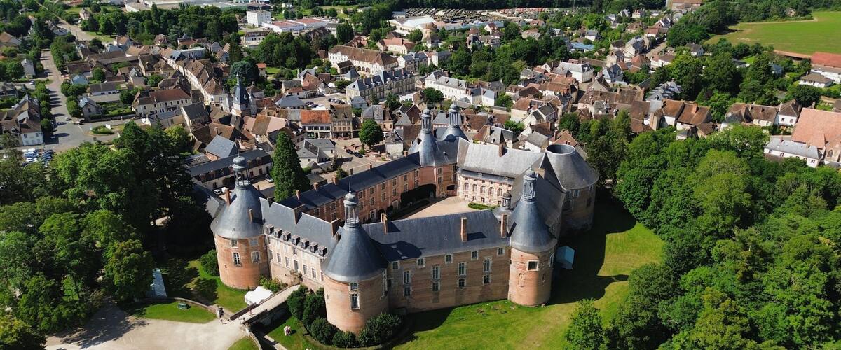 An aerial view of a historic castle surrounded by lush greenery and a small town.
