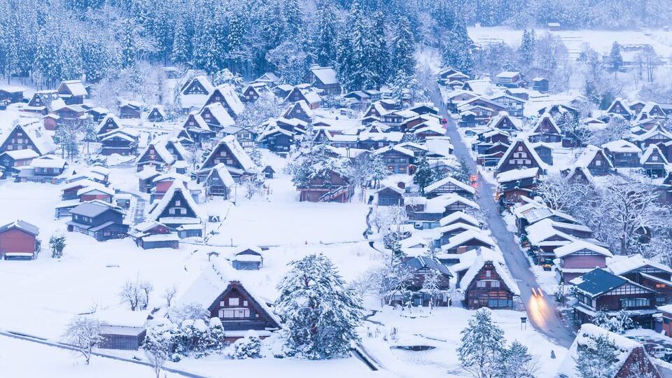 A snow-covered village with traditional wooden houses and a river in the background.