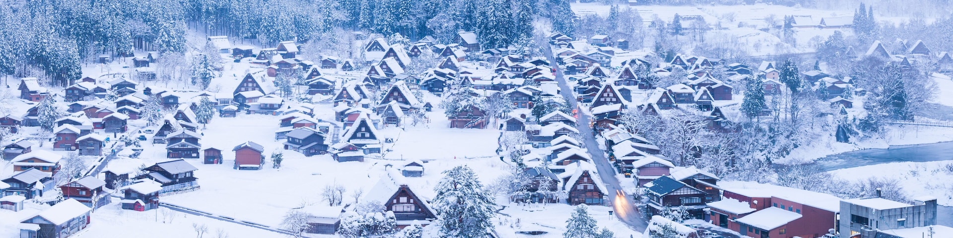 Un pueblo cubierto de nieve con casas de madera tradicionales y un río al fondo.