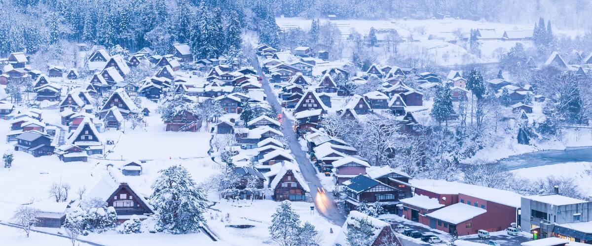 A snow-covered village with traditional wooden houses and a river in the background.
