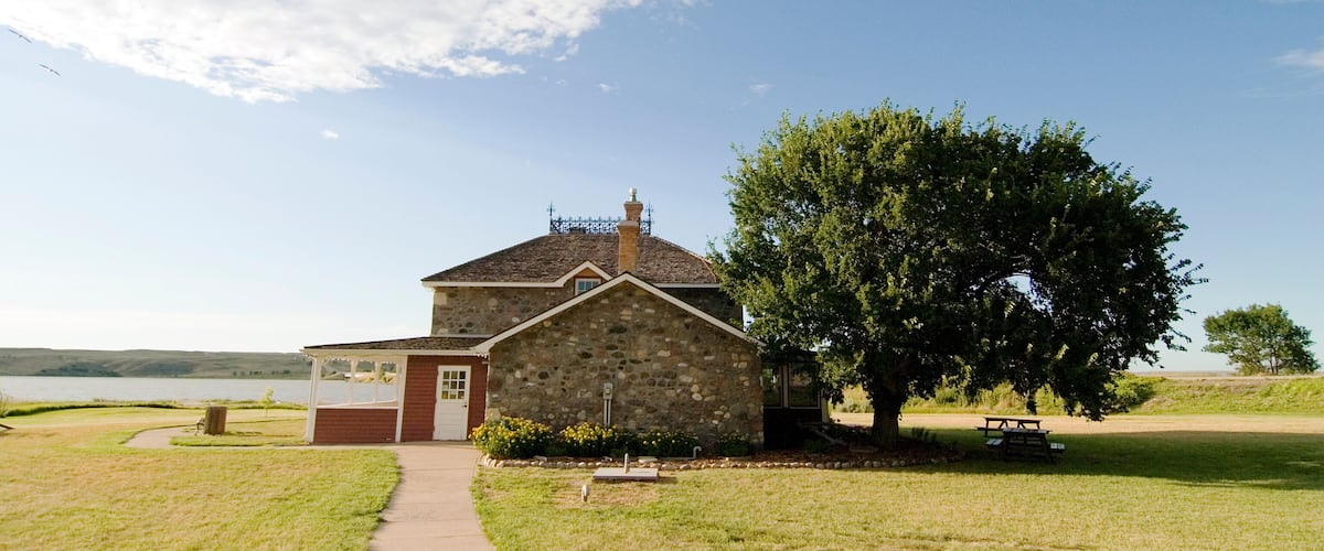 A stone building with a red door, a picnic table, and a large tree in front.