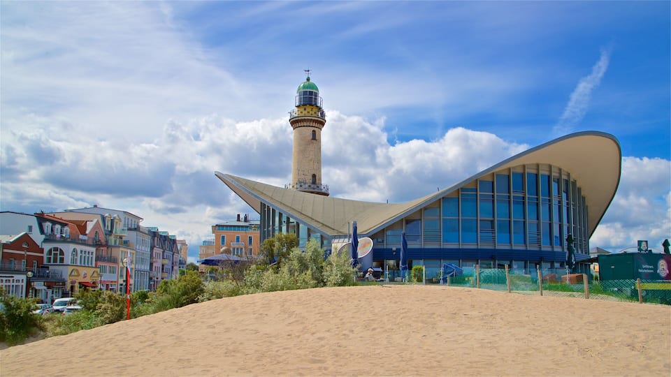 A modern building with a unique curved roof, a tall tower, and a sandy foreground.