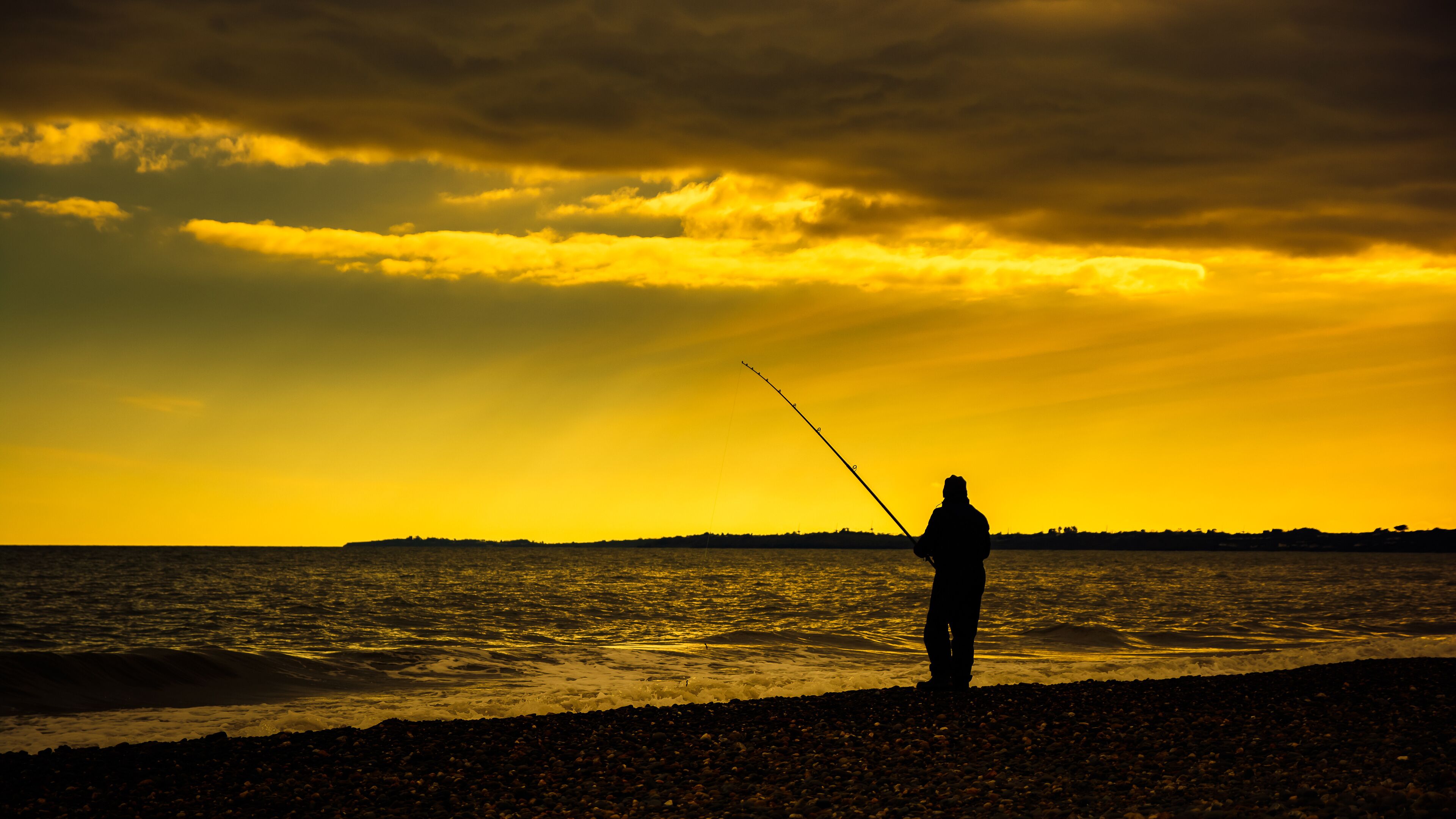A silhouette of a person fishing at sunset by the sea.
