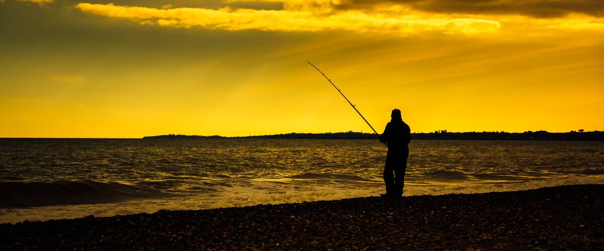A silhouette of a person fishing at sunset by the sea.
