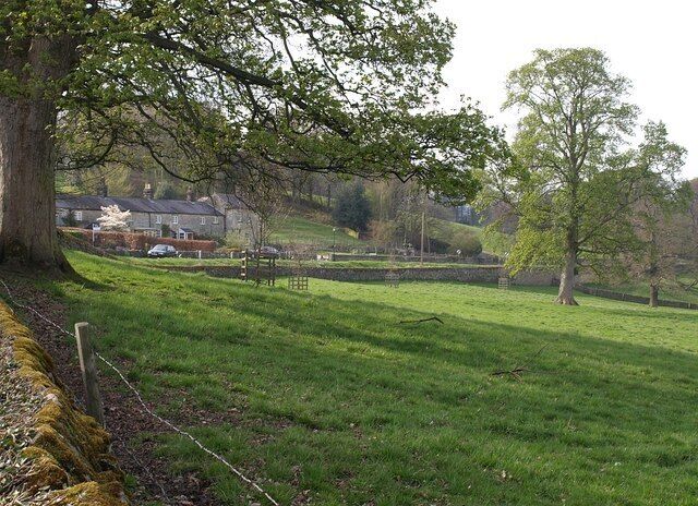 A grassy field with trees and a house in the background.