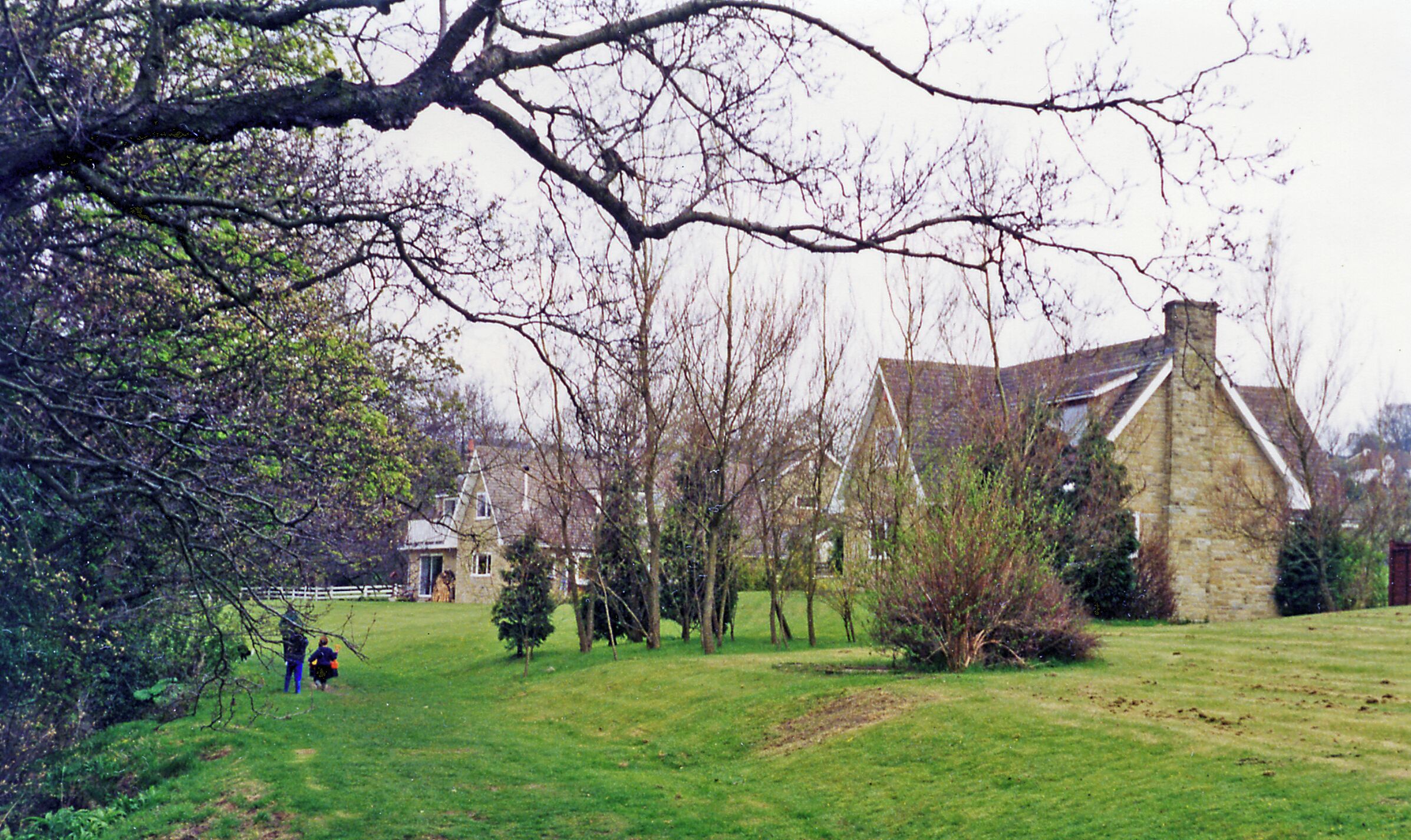 A stone house with a steep roof, surrounded by a grassy field and trees.