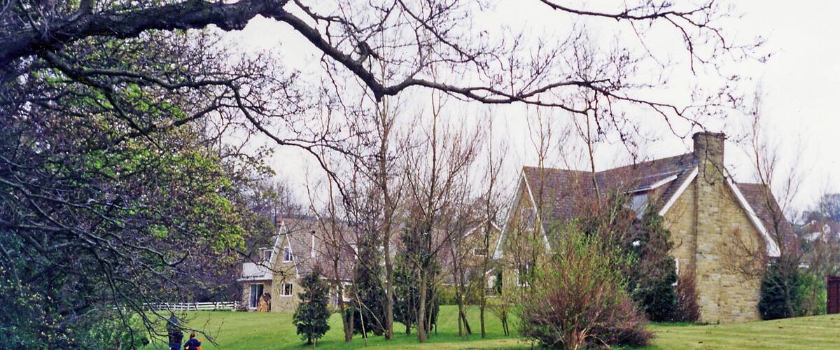 A stone house with a steep roof, surrounded by a grassy field and trees.