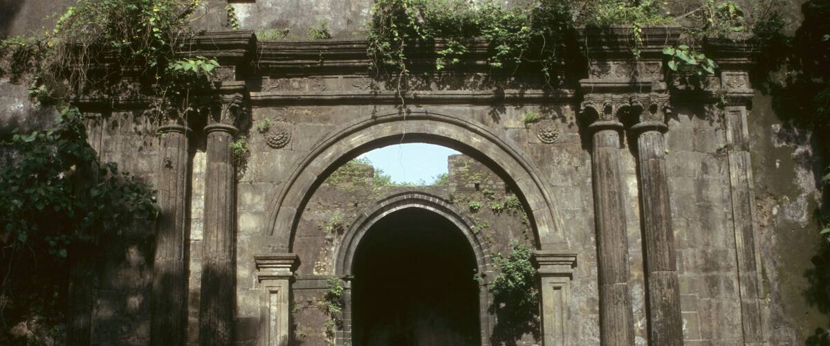 An ancient stone archway with intricate carvings and a grassy area in front.